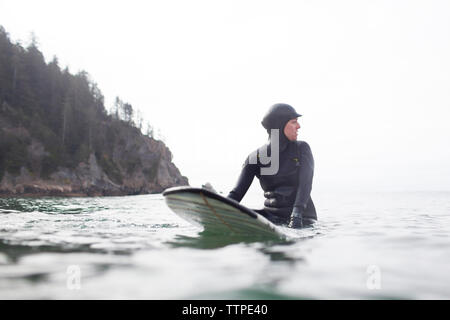 Woman looking over Shoulder, assis sur une planche de surf en mer contre ciel clair Banque D'Images