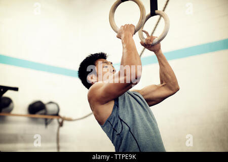 Low angle view of male athlete exerçant sur les anneaux de gymnastique en salle de sport Banque D'Images