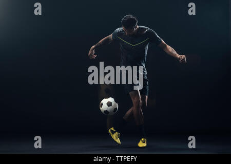 Toute la longueur de soccer player kicking ball sur fond noir Banque D'Images