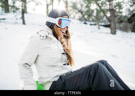 Heureux femme portant des lunettes de ski assis sur le terrain couvert de neige Banque D'Images