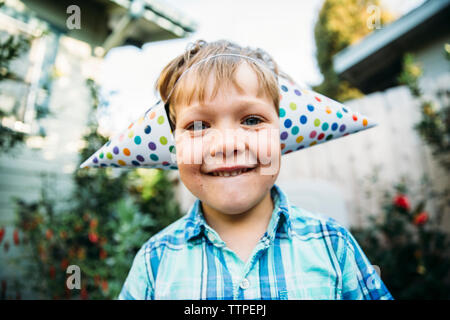 Portrait of happy boy in party hats standing at backyard Banque D'Images