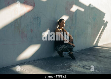 Athlète féminine réfléchie leaning on wall alors que tapi à trottoir Banque D'Images