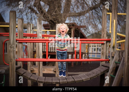 Jeune garçon rire et jouer sur l'aire de jeux dans un parc Banque D'Images