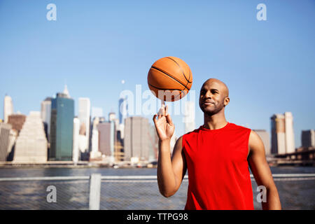 Smiling man spinning basket-ball sur le doigt contre city skyline Banque D'Images