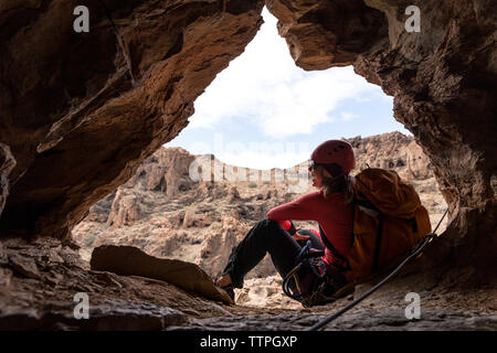 Femmes gaies backpacker assis sur entrée de caverne dans rock formation Banque D'Images