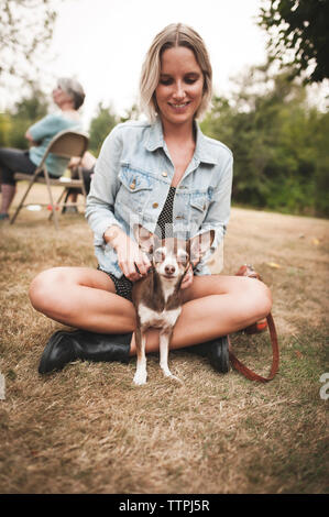 Smiling woman Playing with Chihuahua while sitting on grassy field in yard Banque D'Images