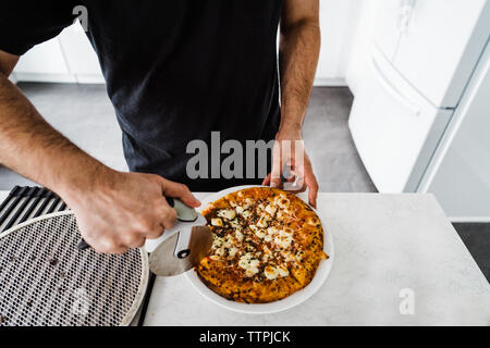 Man's hands slicing pizza au fromage Banque D'Images
