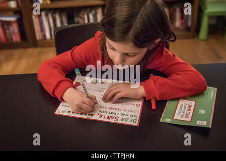 Mignonne fille écrivant lettre au Père Noël à la maison pendant noël Banque D'Images