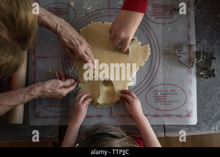 Les mains coupées de petits-enfants et grand-mère avec la pâte de coupe emporte-pièces sur la table à la maison Banque D'Images