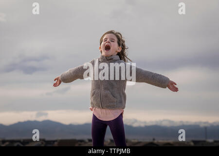 Happy girl with arms outstretched hurlant debout contre ciel nuageux