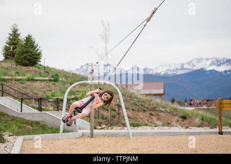 Happy girl wearing sunglasses pendant la rotation de la chaîne de montagnes à swing contre park Banque D'Images