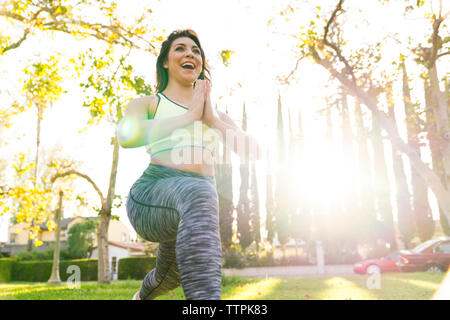 Low angle view of cheerful woman practicing yoga tout en s'exerçant dans la région de Park au cours de journée ensoleillée Banque D'Images