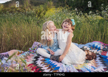 Cheerful sisters sitting on blanket in park Banque D'Images