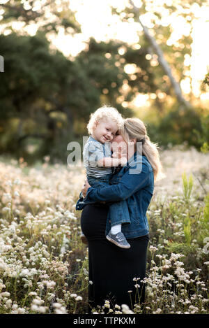 Pregnant woman kissing son tout en se tenant au milieu de plantes Banque D'Images