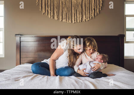 Mère regardant bébé fille porté par sa fille sur le lit chez lui Banque D'Images