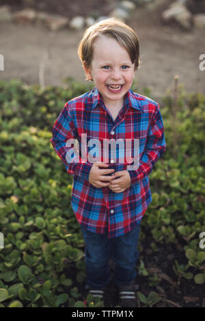 Full Length portrait of smiling boy standing au milieu d'usines à park Banque D'Images