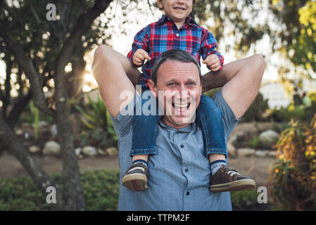 Portrait of cheerful father carrying son sur les épaules tout en jouant avec lui à park Banque D'Images