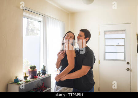 Happy couple standing by window at home Banque D'Images