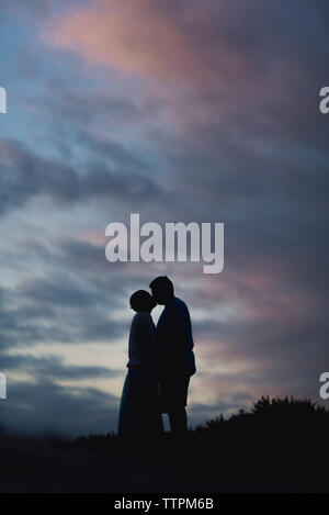 Silhouette couple en se tenant sur le terrain contre ciel nuageux pendant le coucher du soleil Banque D'Images