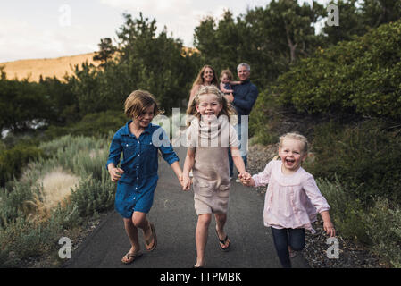 Les parents à la recherche de happy filles tenant la main tout en courant sur route contre trees in forest Banque D'Images