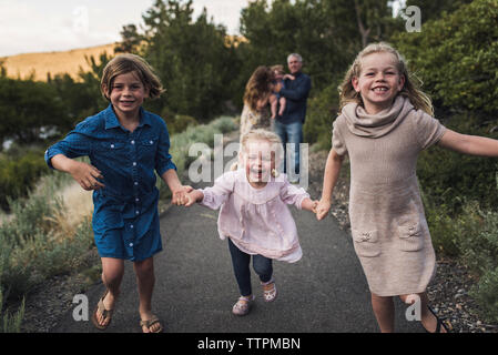 Heureux soeurs tenant la main tout en courant sur la route contre les parents en forêt Banque D'Images