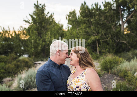 Happy romantic couple rubbing noses debout contre des arbres en forêt Banque D'Images