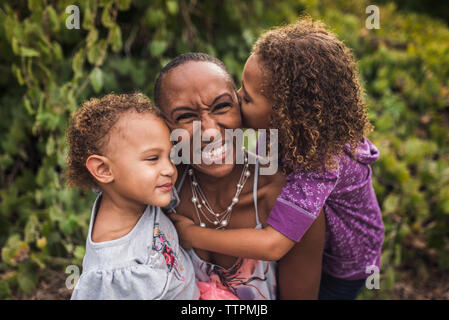 High angle portrait of happy mother and daughters assis contre des plantes dans le parc Banque D'Images