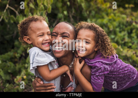 Portrait de mère heureuse avec filles assis contre des plantes dans le parc Banque D'Images