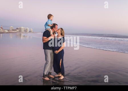 Mari Femme embrasser tout en portant son on shoulders at beach against clear sky pendant le coucher du soleil Banque D'Images