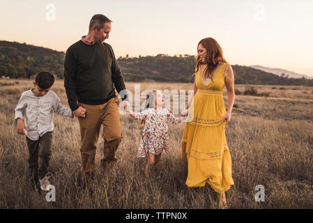 Jeune famille tenant la main tout en marchant en Californie field at sunset Banque D'Images