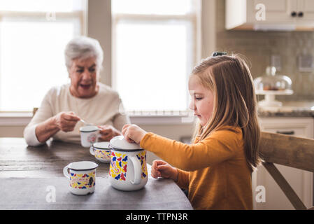 Petite-fille et grand-mère dans la cuisine à jouer avec un service à thé Banque D'Images