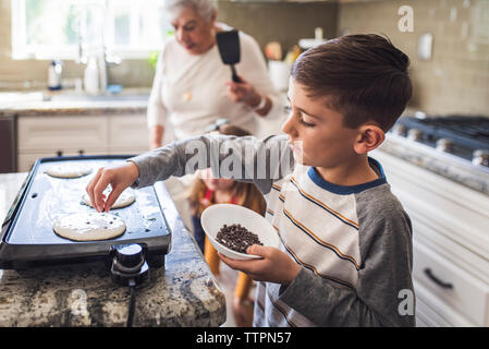 Jeune garçon la cuisson des crêpes avec famille de plusieurs générations Banque D'Images