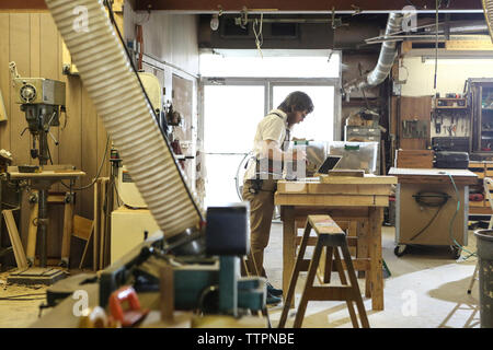 Vue de côté de carpenter l'examen de planche en bois à l'établi dans l'atelier Banque D'Images