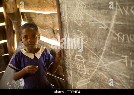 Portrait of Girl standing by blackboard in classroom Banque D'Images