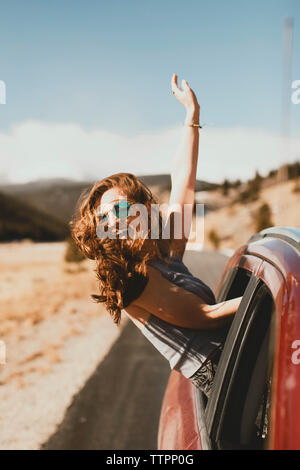 Cheerful jeune femme avec des cheveux ébouriffés incliné vers l'extérieur à partir de la fenêtre de voiture Banque D'Images