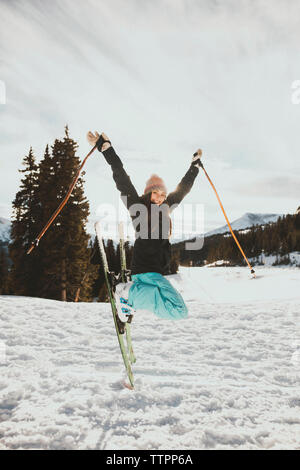 Young woman jumping excité en skiant sur champ neigeux Banque D'Images