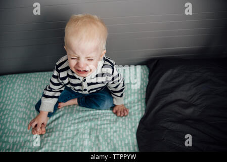 Portrait of boy crying while sitting on bed at home Banque D'Images