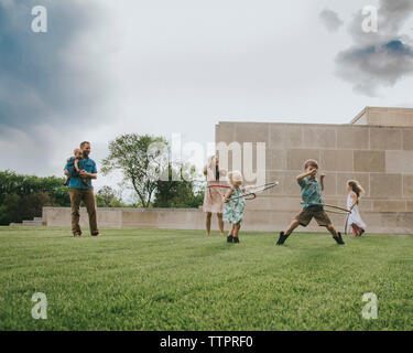 Père des enfants jouant avec Hula Hoop sur terrain against sky Banque D'Images