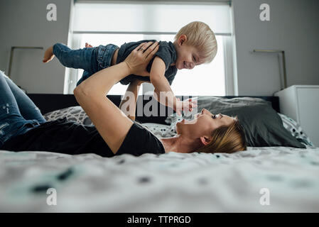 Vue latérale d'heureux mère ramasser des fils en position couchée sur le lit chez lui Banque D'Images