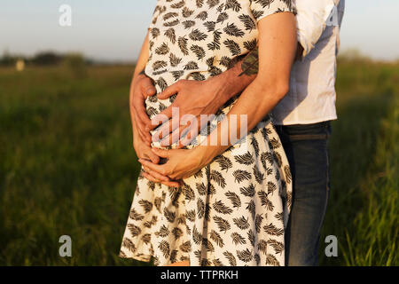 Portrait de l'homme touchant l'estomac de la femme enceinte en se tenant sur le terrain herbeux Banque D'Images