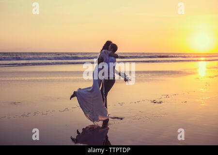 Senior couple embracing at beach against clear sky pendant le coucher du soleil Banque D'Images
