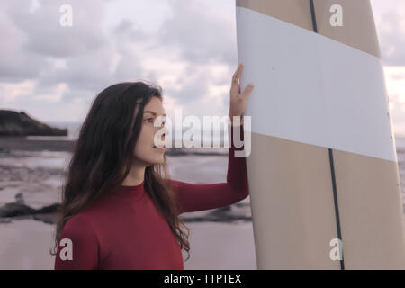 Young woman with surfboard standing at beach Banque D'Images