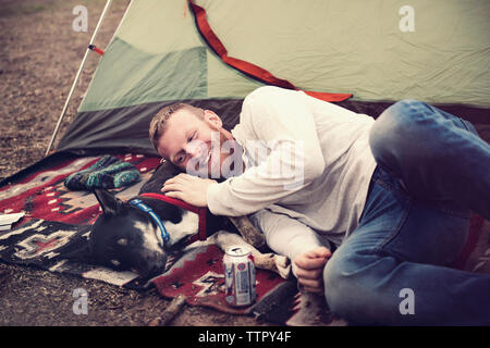 Heureux homme étendu sur chien à l'extérieur de la tente à camp site Banque D'Images