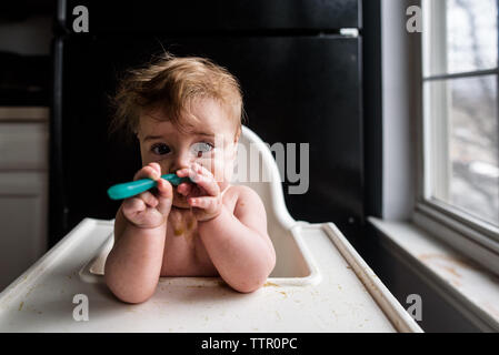 Gros plan de bébé en désordre de manger avec une cuillère dans une chaise haute Banque D'Images