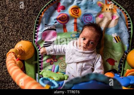 Jeune bébé portant sur tapis de jeu à la recherche jusqu'à jouets pendant vers le bas Banque D'Images