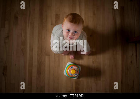 Overhead portrait of cute baby boy with toy assis sur le plancher à la maison Banque D'Images