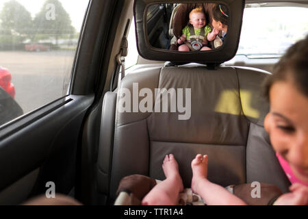 Réflexion de sœur jouant avec le frère vu in back seat mirror Banque D'Images