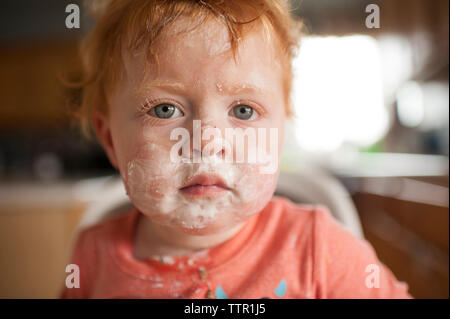 Close-up portrait of cute baby boy with messy face sitting sur la chaise haute à la maison Banque D'Images