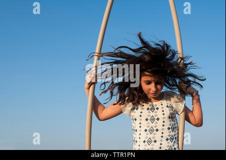 Fille avec des cheveux ébouriffés jouer contre ciel bleu clair à l'aire de jeux Banque D'Images