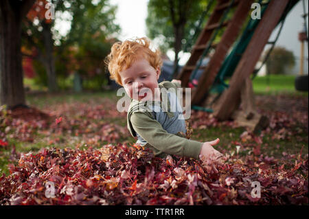 Bébé garçon joyeux joue dans la pile de feuilles dans la cour à la maison Banque D'Images